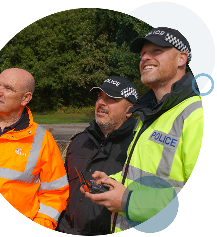 A circular image of three men partaking in emergency service drone training.