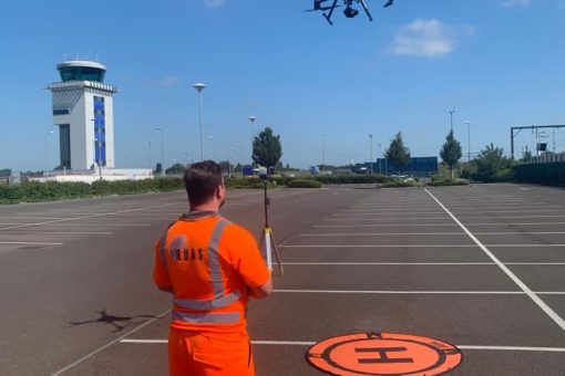 A man wearing a high vis suit with the RUAS logo on it, at Southend Airport RPZ, flying a drone.